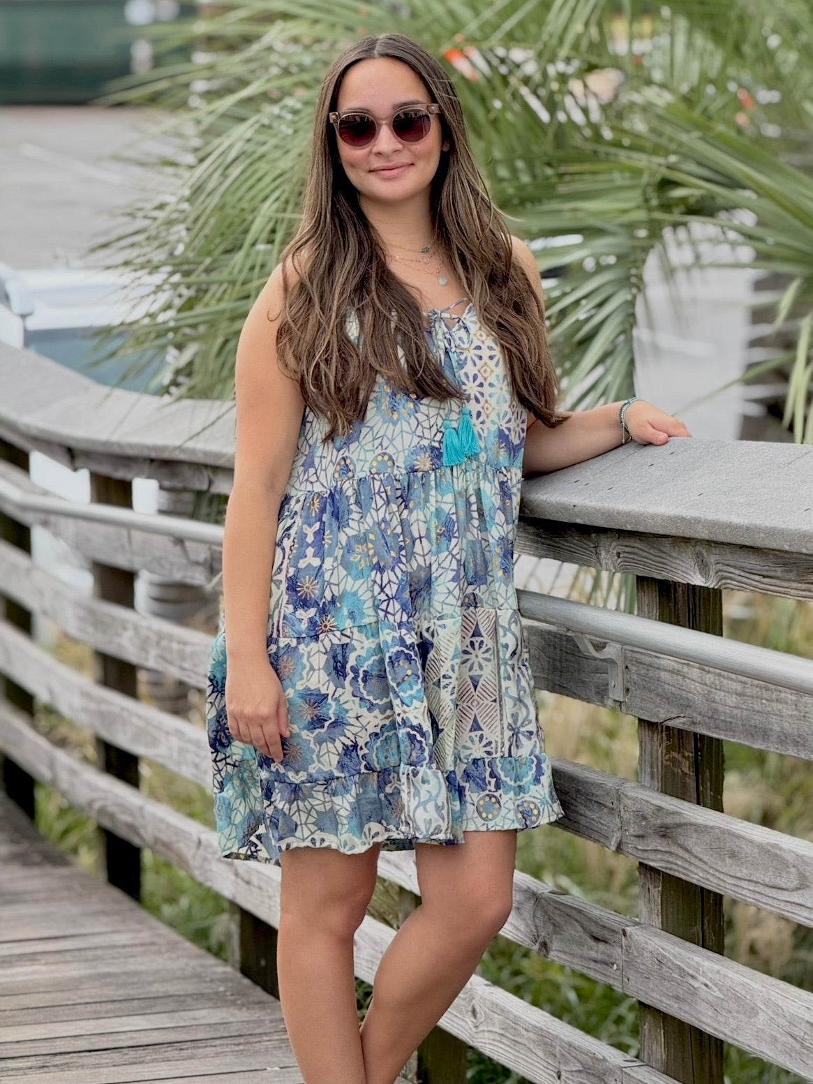 Woman in a floral dress standing on a wooden deck with greenery in the background