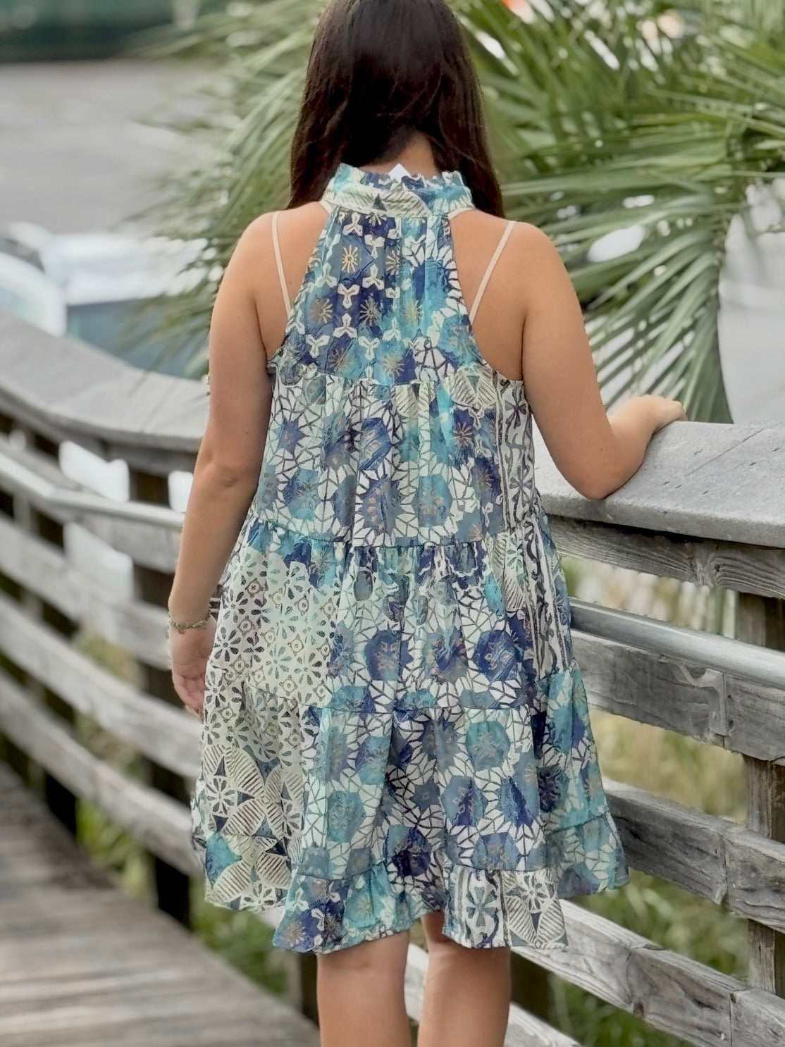Woman wearing a floral dress standing on a wooden bridge with greenery in the background