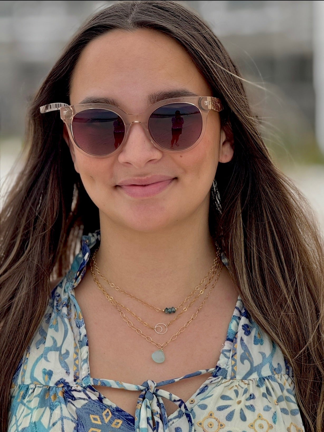 Woman wearing sunglasses and a floral top with layered necklaces outdoors