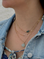 Close-up of a person wearing layered gold necklaces with a denim jacket and colorful top.