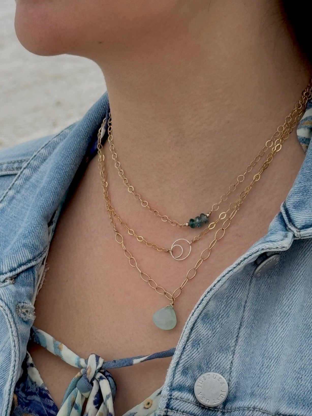 Close-up of a person wearing layered gold necklaces with a denim jacket and colorful top.