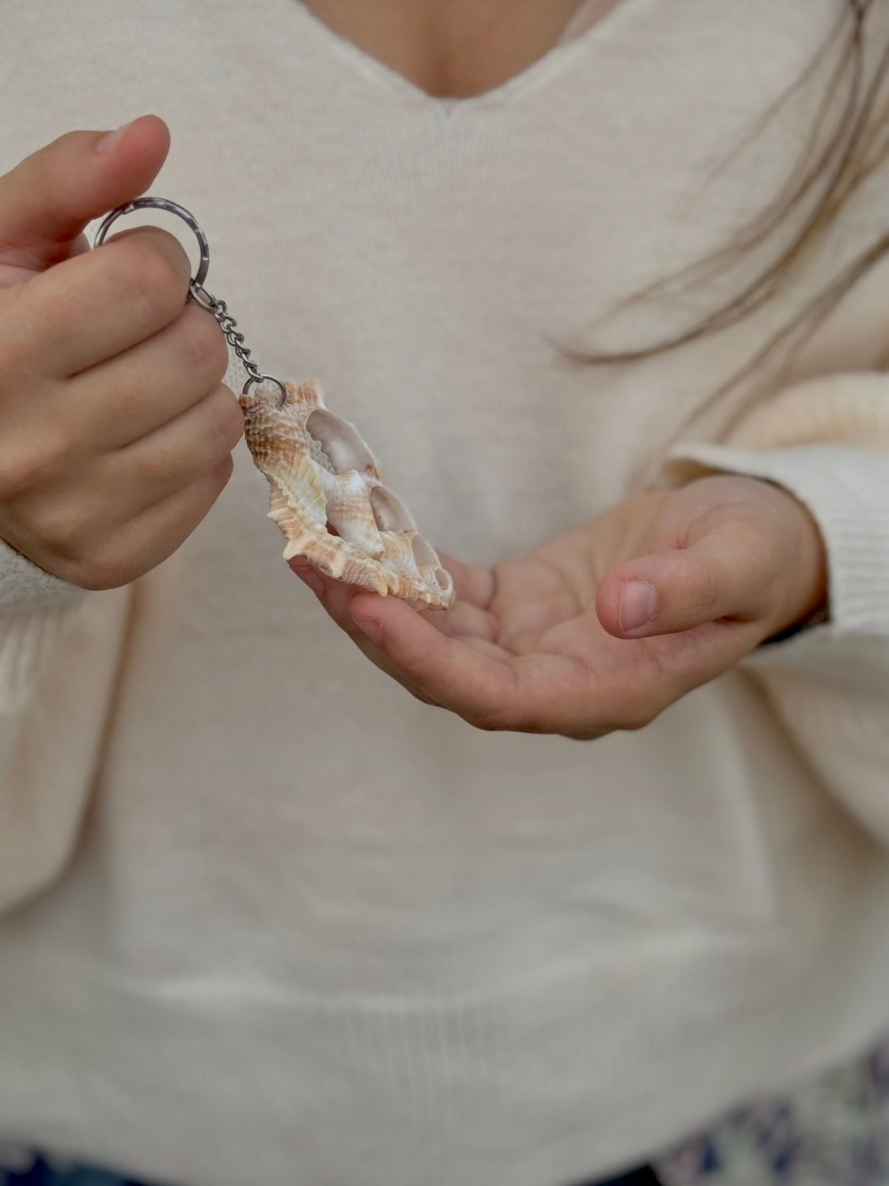 Person holding a keychain with a natural cut seashell against a neutral background