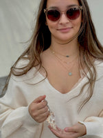 Woman wearing sunglasses and layered necklaces, holding a shell keychain.