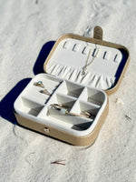 Elizabeth Jewelry Case in gold resting on white sand, displaying jewelry arranged inside the soft velvet compartments.