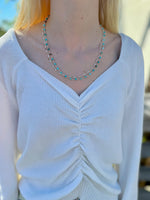 Person wearing a white sweater and turquoise beaded necklace outdoors