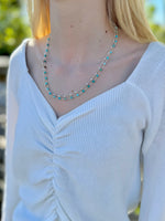 Person wearing a white sweater and turquoise beaded necklace outdoors