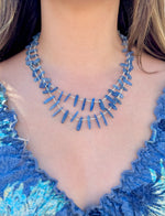 Blue beaded necklace worn by a person in a blue textured top.