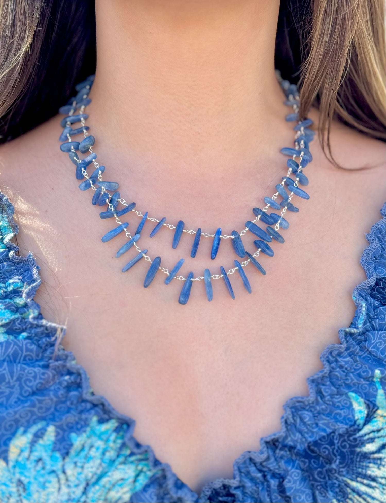Blue beaded necklace worn by a person in a blue textured top.