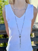 Person wearing a white sleeveless top with a long necklace, standing outdoors.