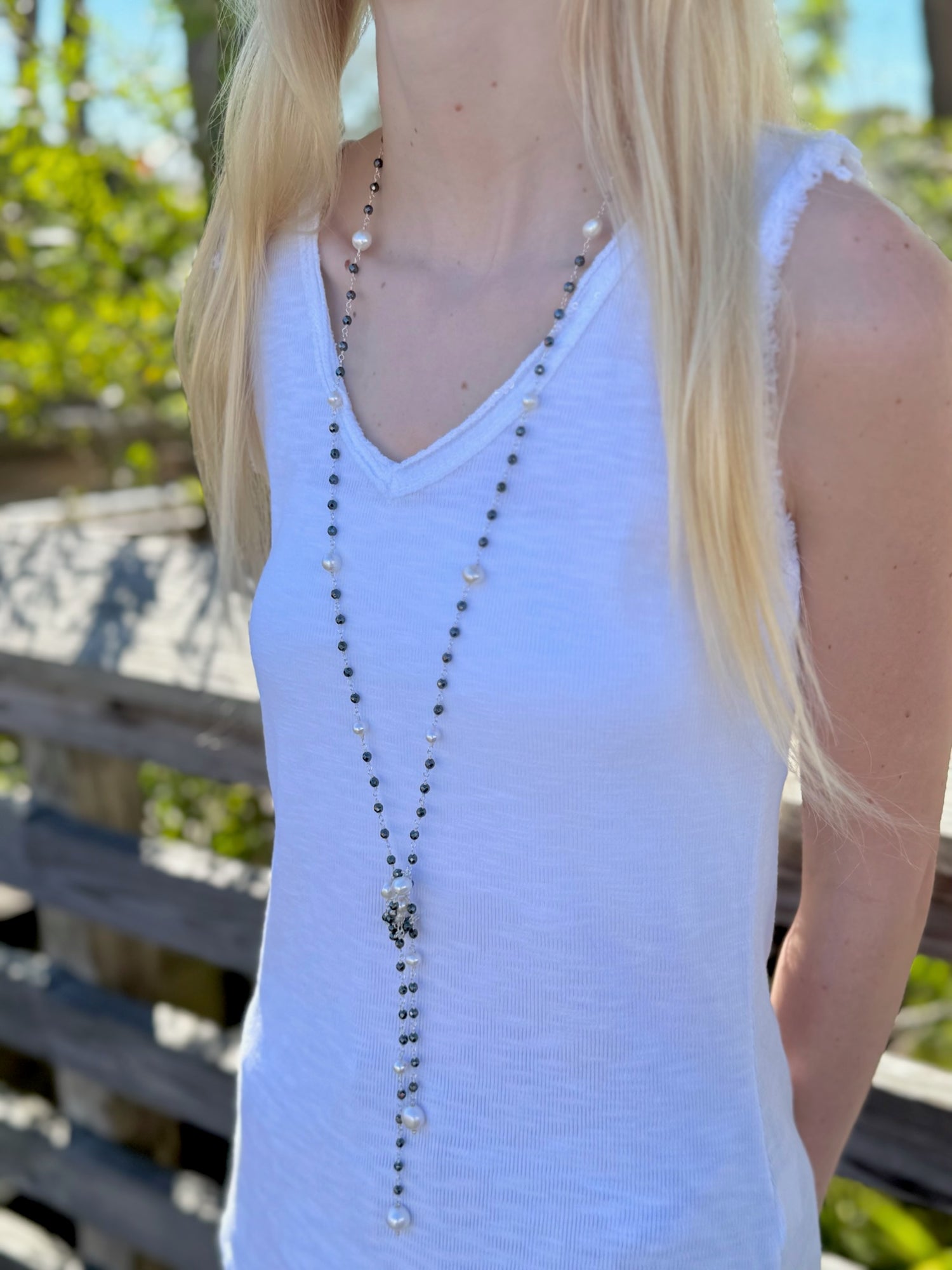 Person wearing a white tank top with a long necklace outdoors