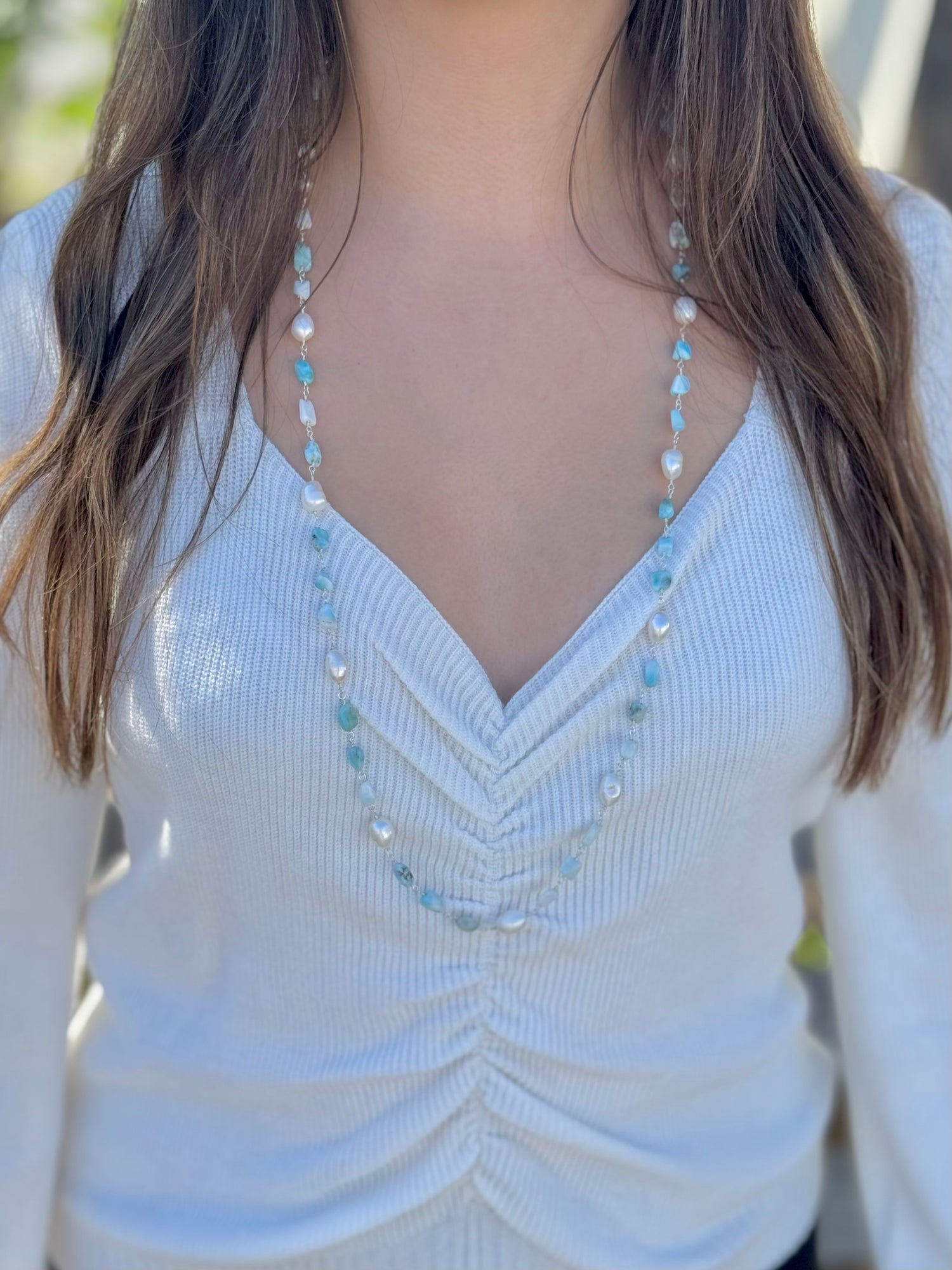 Close-up of the Adrina Amazonite and Freshwater Pearls sterling silver necklace draped on a woman in a white ruched sweater.