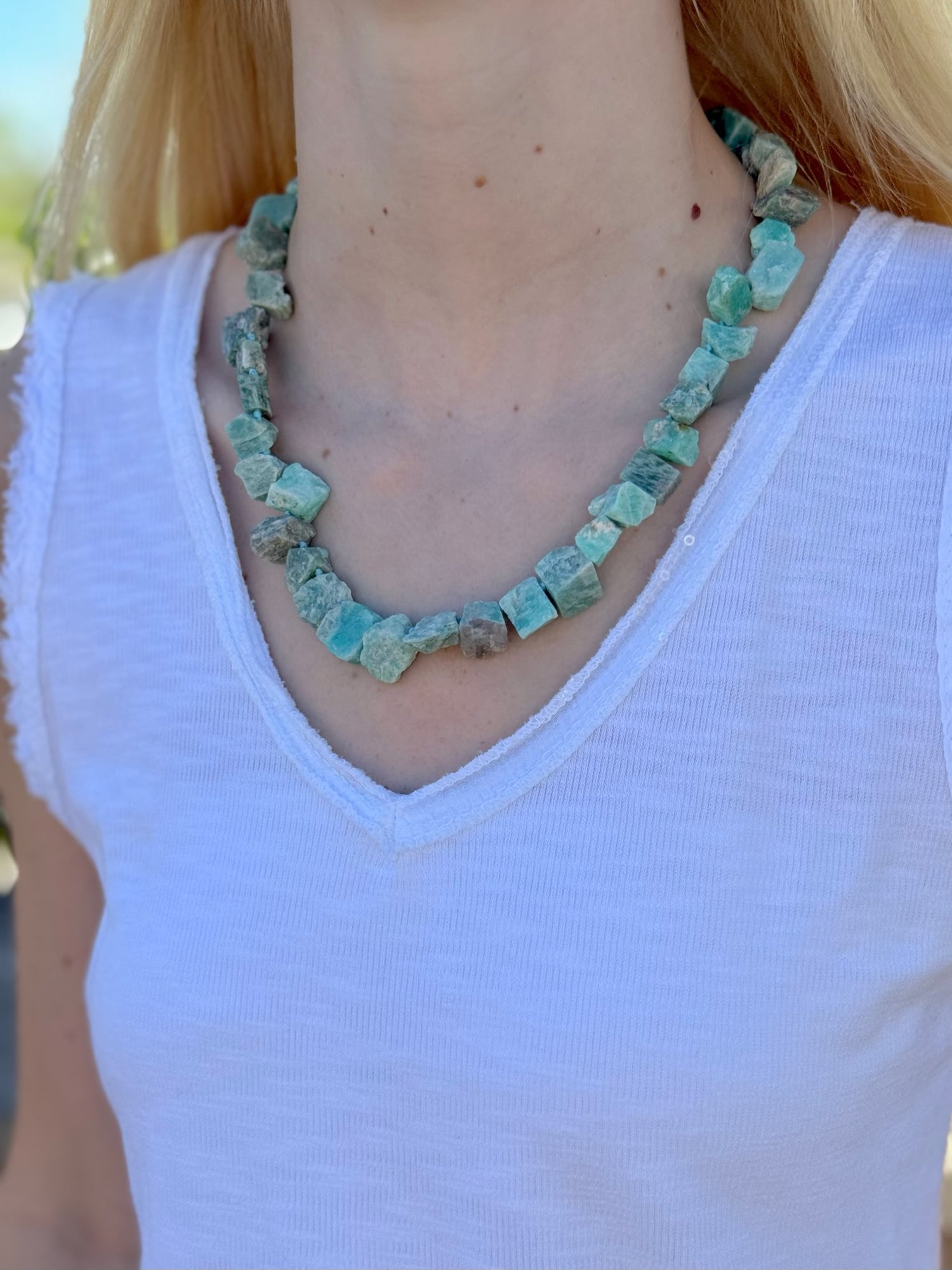 Person wearing a green gemstone necklace against a blurred outdoor background