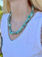 Person wearing a turquoise beaded necklace with a white top.