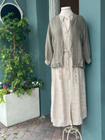 Taupe linen zip-front jacket with ribbed collar and cuffs, side pockets, and adjustable drawstring hem details, layered over a natural linen dress.