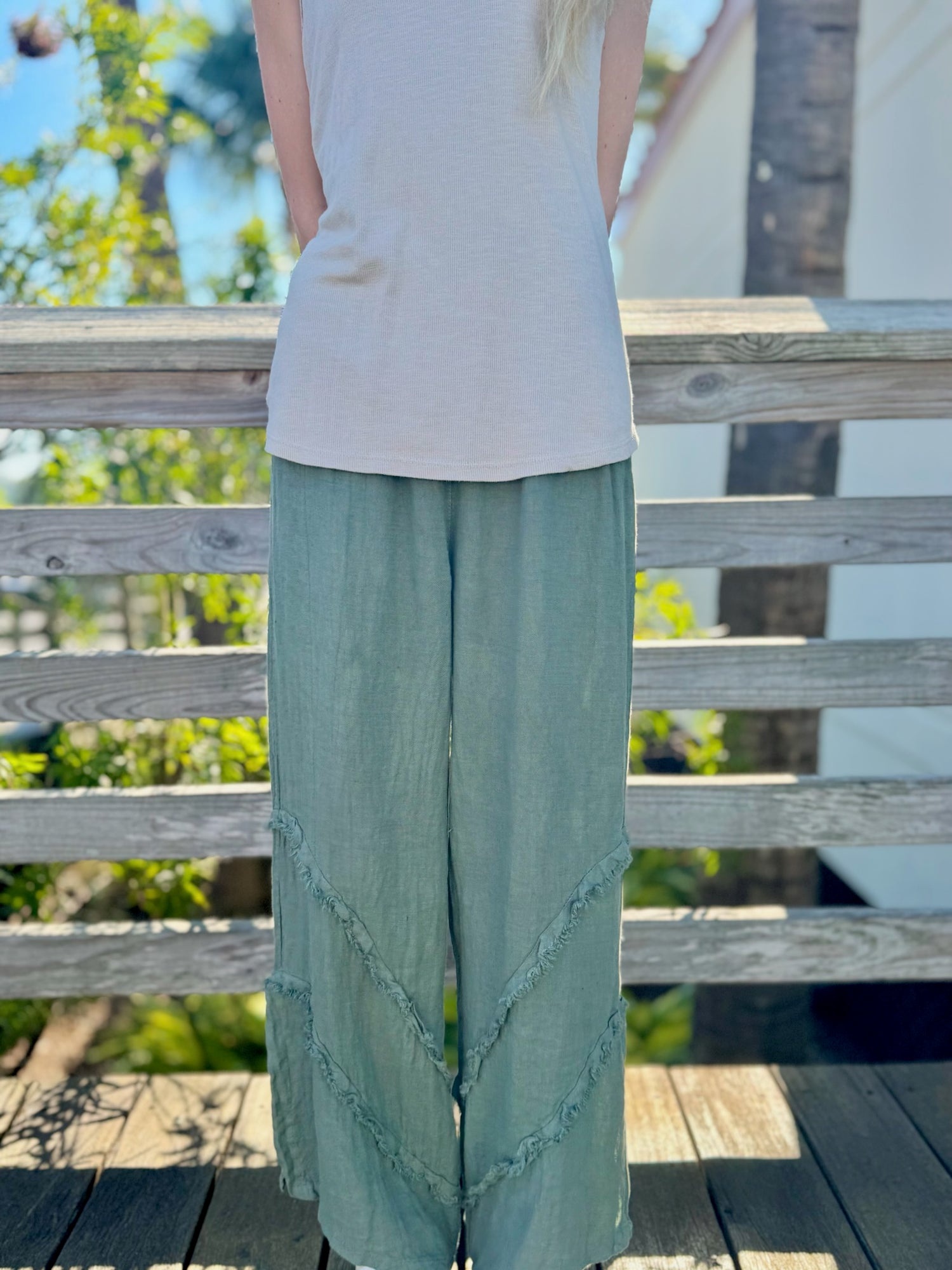 Front view of model wearing olive wide-leg linen pants with raw-edge diagonal seams.