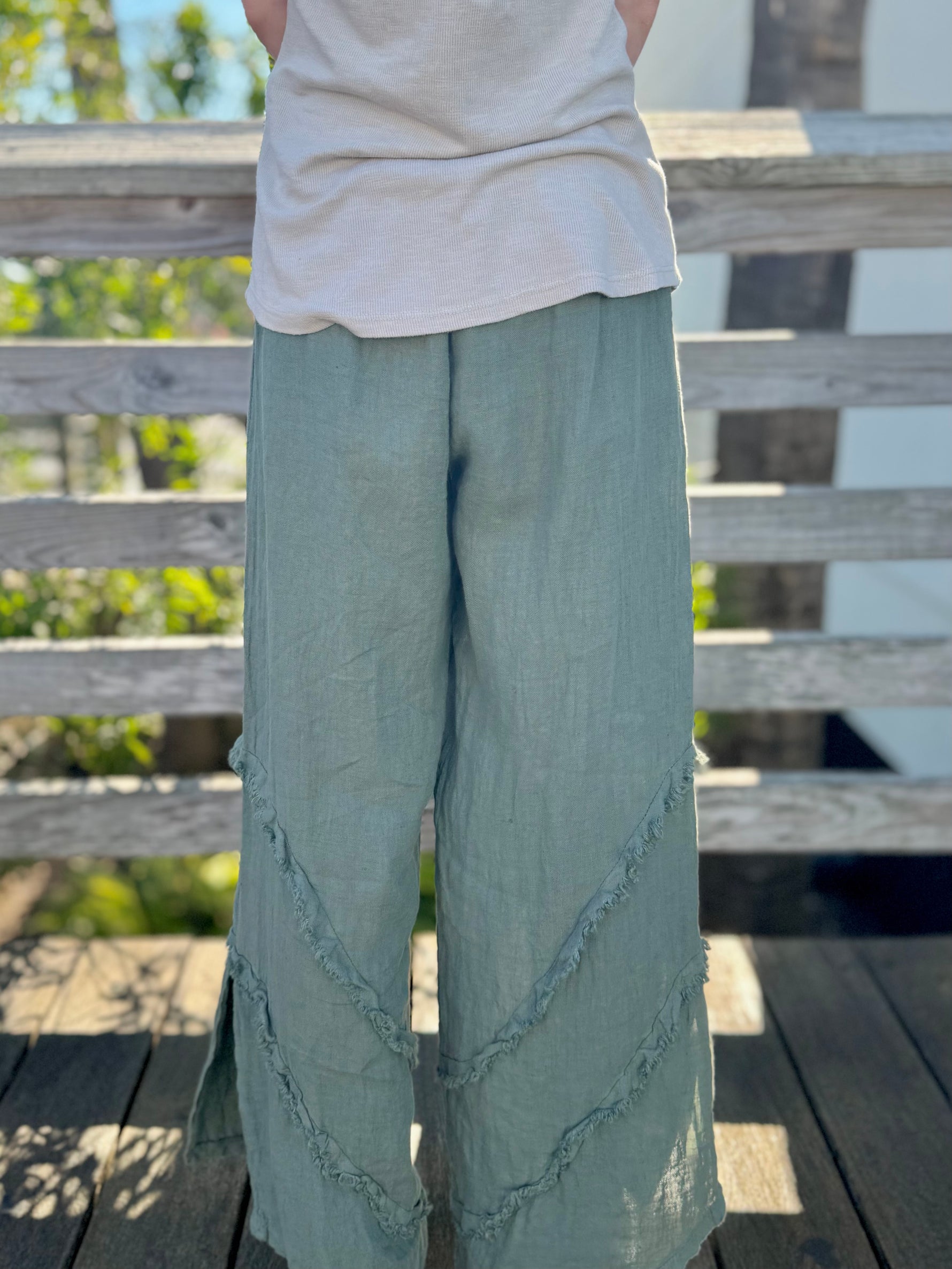 Back angle view of wide-leg olive linen pants with subtle frayed detailing.