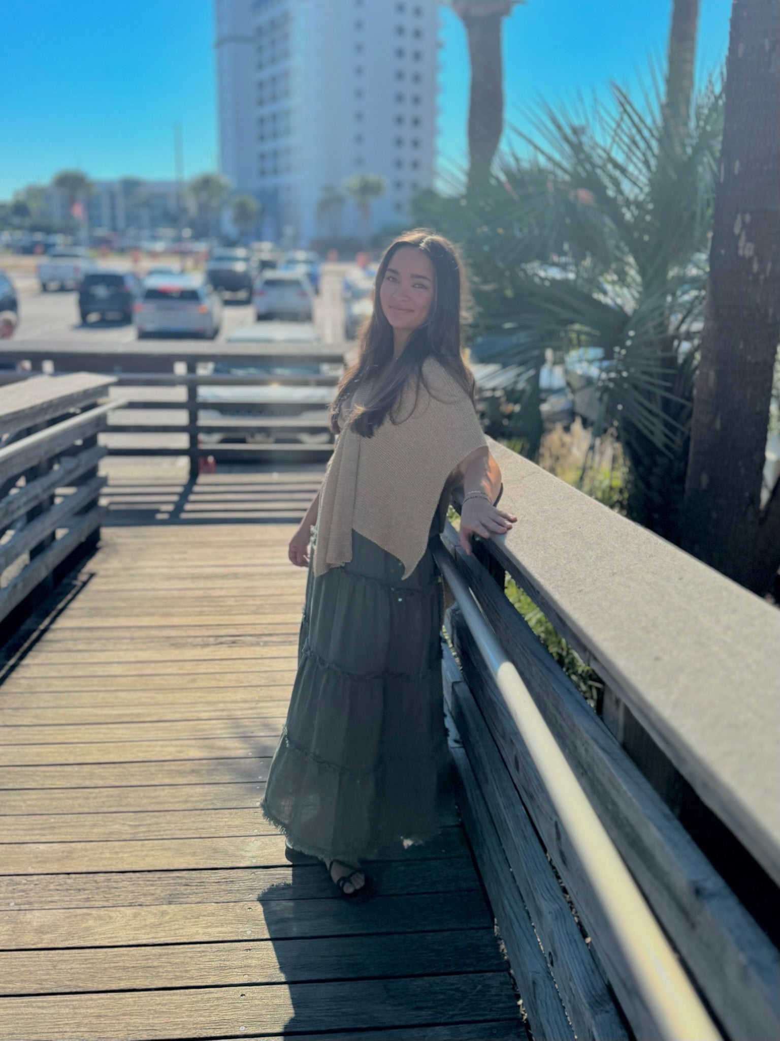 Woman standing on a wooden boardwalk with a cityscape and palm trees in the background