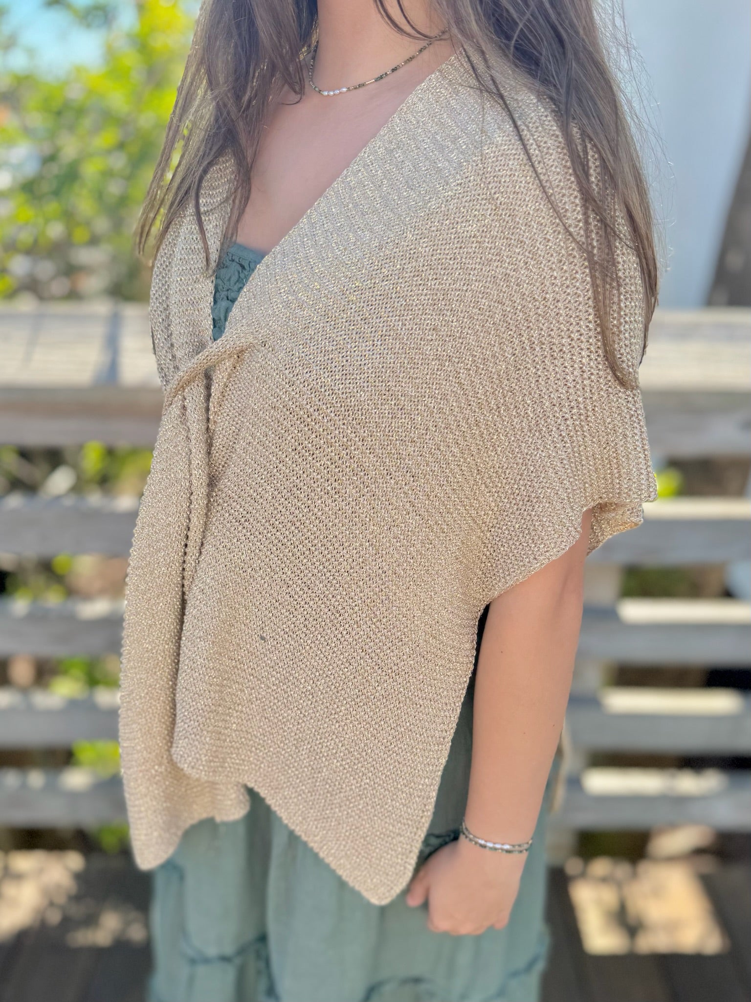 Person wearing a gold knitted shrug over a light green dress outdoors.