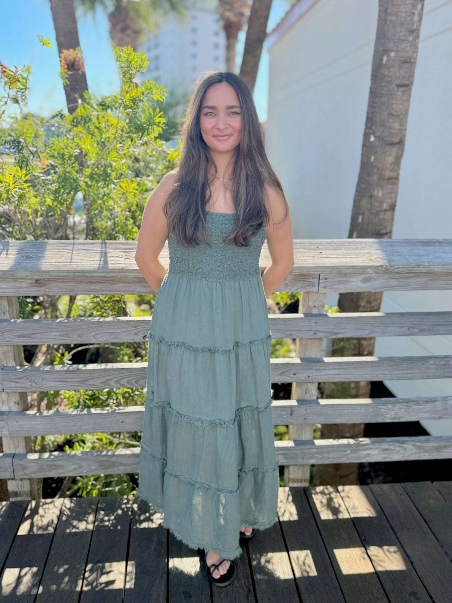 Woman in a green dress standing on a wooden deck with trees and buildings in the background