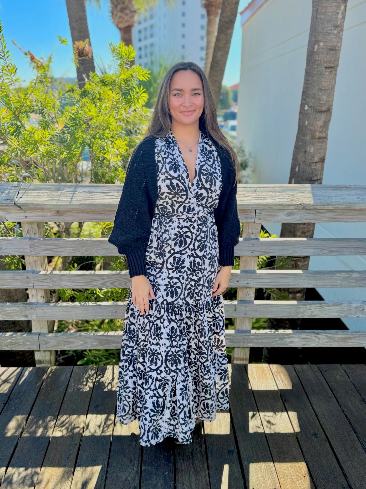 Side view of a woman wearing a black knit shawl with textured open-stitch detailing over a patterned dress.
