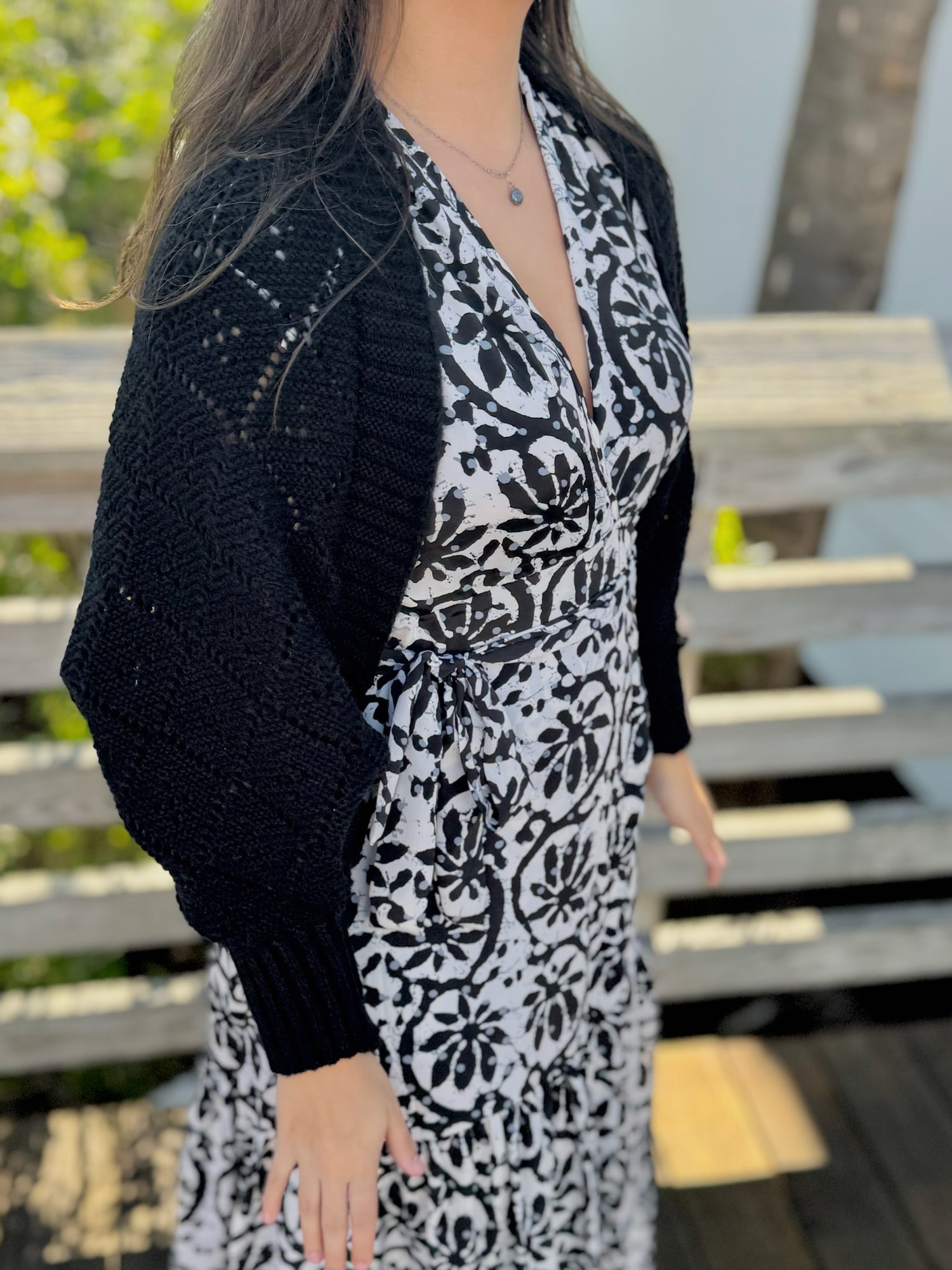 Side view of a woman wearing a black knit shawl with textured open-stitch detailing over a patterned dress.