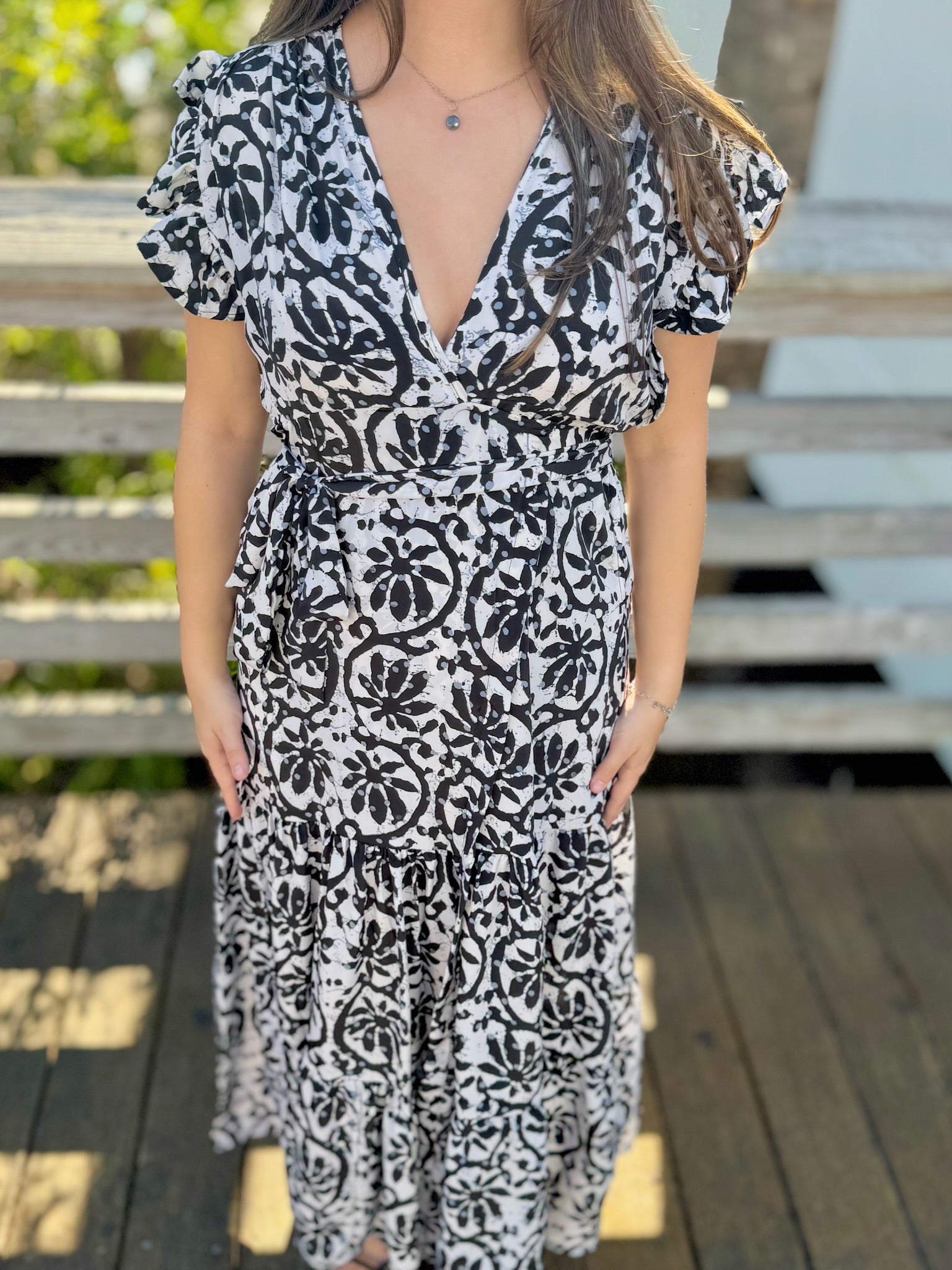 Front view of a woman wearing a black-and-white printed wrap dress with ruffled sleeves and a tiered skirt.