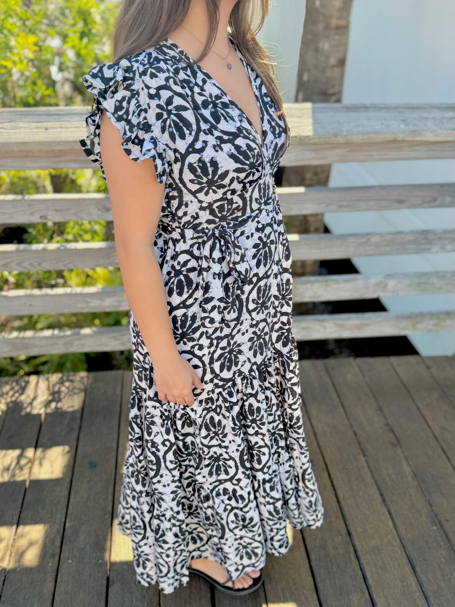 Side view of a woman wearing a black-and-white printed wrap dress, showing the flutter sleeves and tied waist detail.
