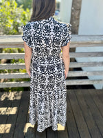 Back view of a black-and-white printed wrap dress with ruffled sleeves and a flowing tiered skirt.