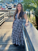 Woman standing outdoors in a black-and-white printed wrap dress with a deep V-neckline, smiling and resting her arm on a railing.