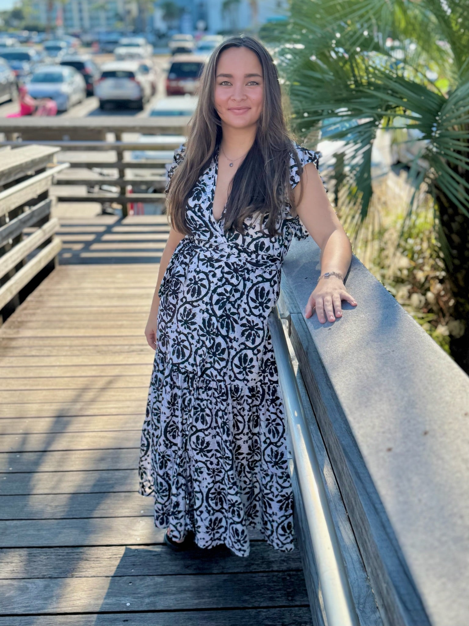 Woman standing outdoors in a black-and-white printed wrap dress with a deep V-neckline, smiling and resting her arm on a railing.