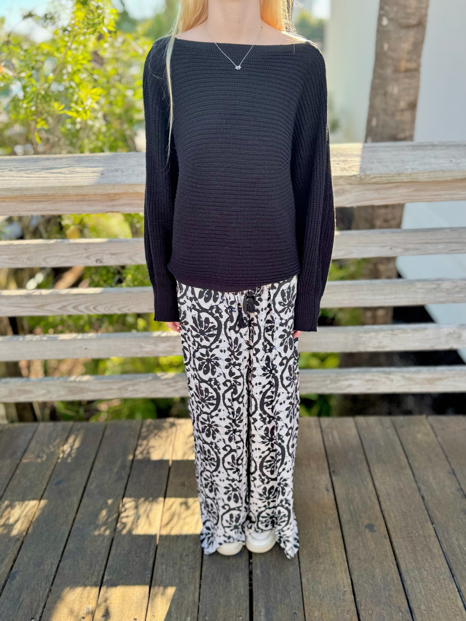 Model wearing black wide-leg pants with a black sweater, showcasing the full relaxed fit and drape of the printed pants.