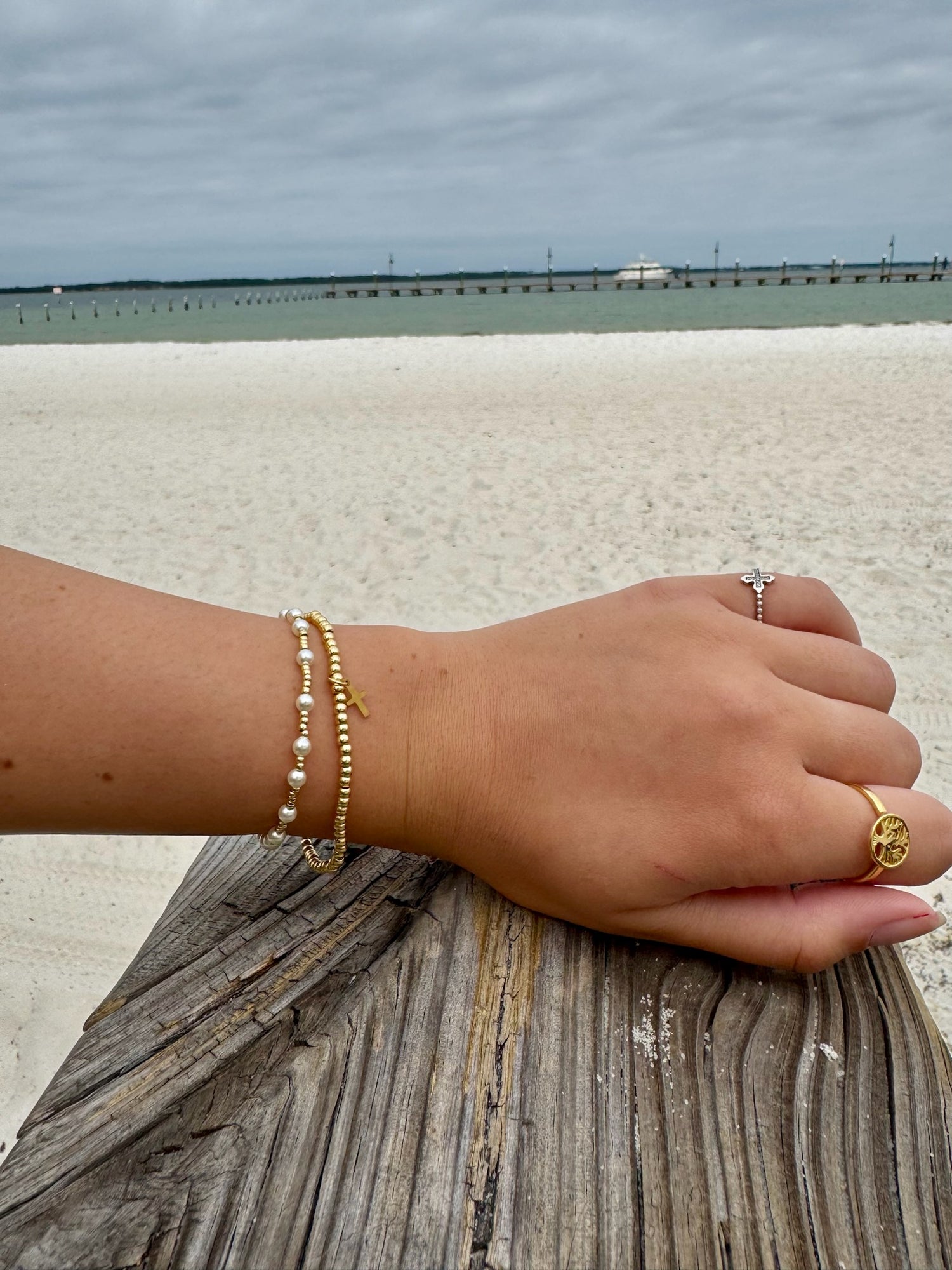 Hand with pearl bracelet and ring on a wooden post by the beach