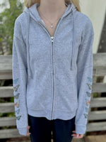 Person wearing a gray hoodie with butterfly designs on sleeves against a wooden background