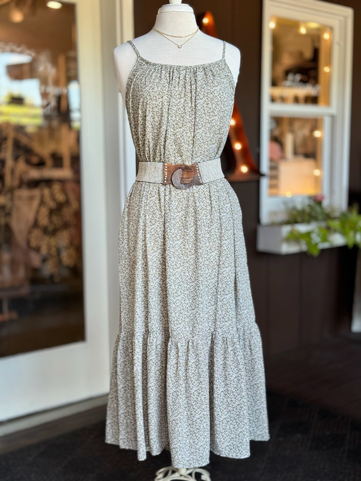 Olive green and white floral maxi dress styled with a brown waist belt, gathered neckline and ruffled hem at Ardor Boutique.