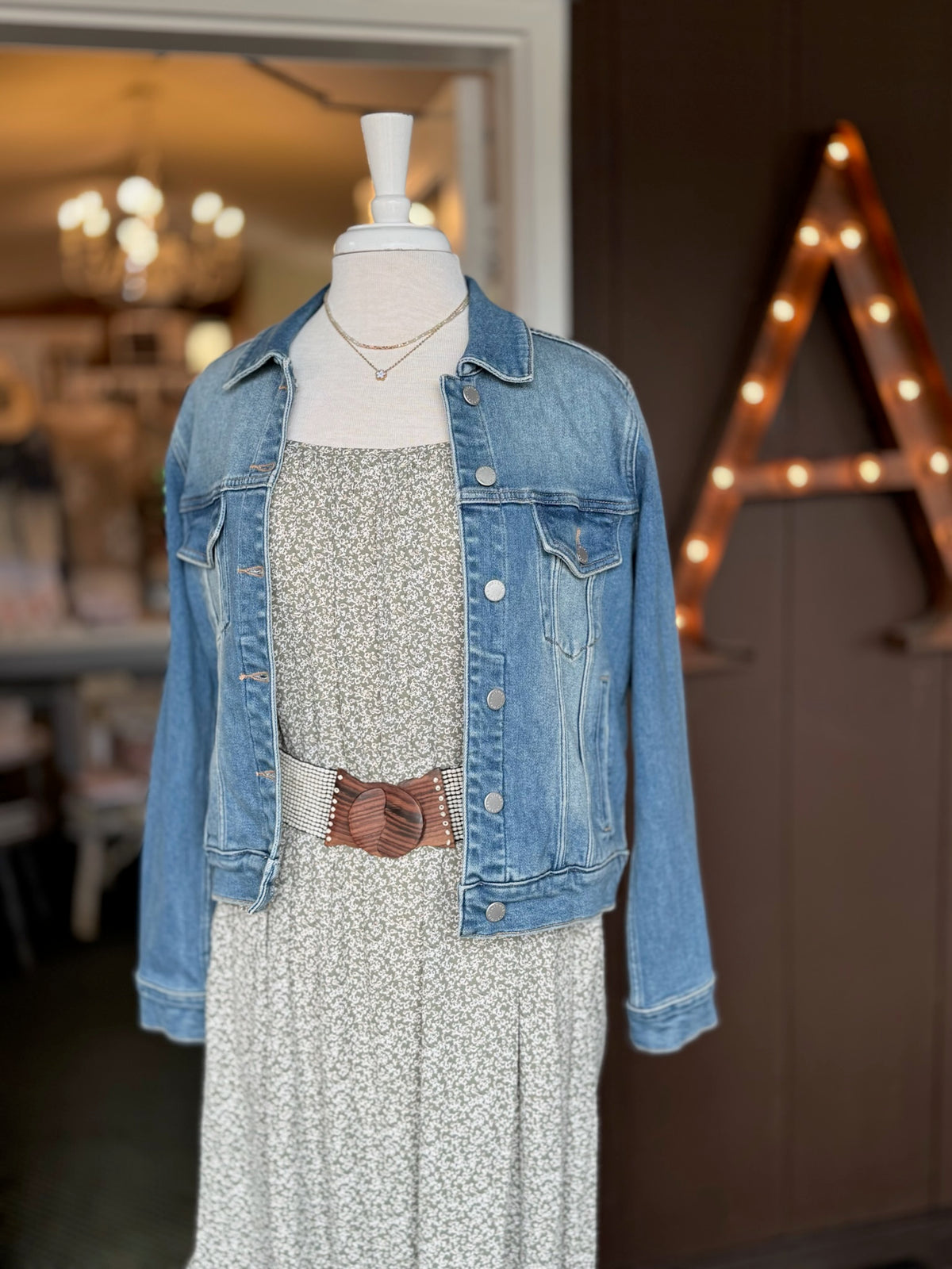 Kinsley Dress in a soft green floral print styled with a medium wash denim jacket, layered necklace, and natural wood buckle belt at Ardor Boutique.