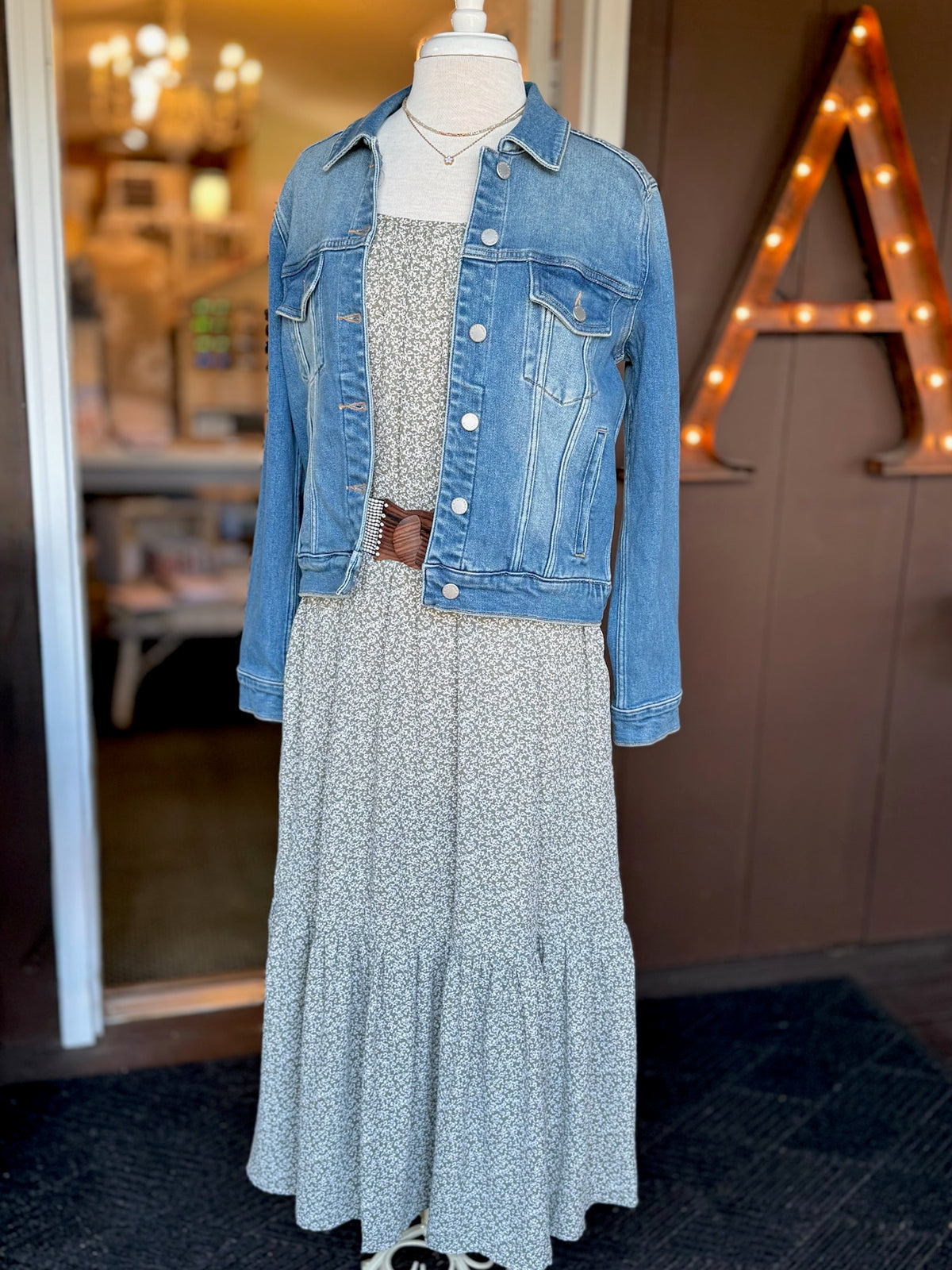 Olive green and white floral maxi dress styled with a blue denim jacket and brown waist belt for transitional weather at Ardor Boutique.