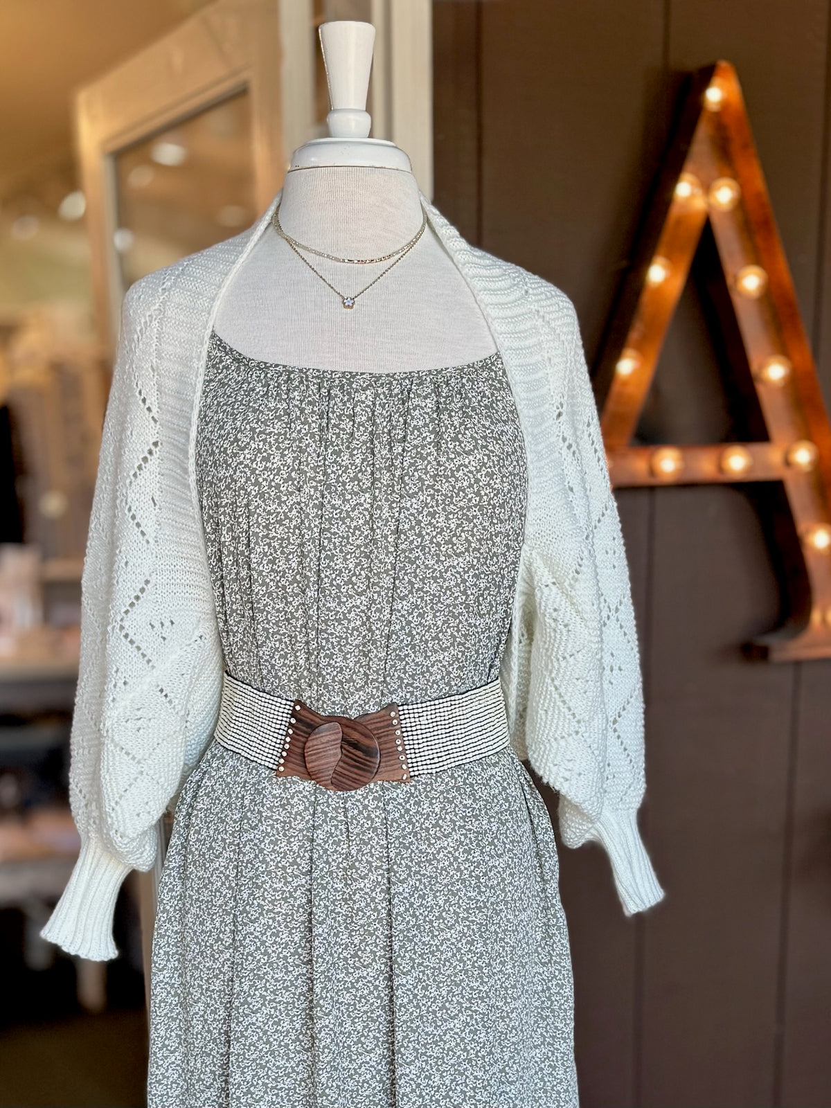 Close-up of ivory open-knit cardigan with textured diamond pattern and ribbed trim layered over a floral dress at Ardor Boutique.