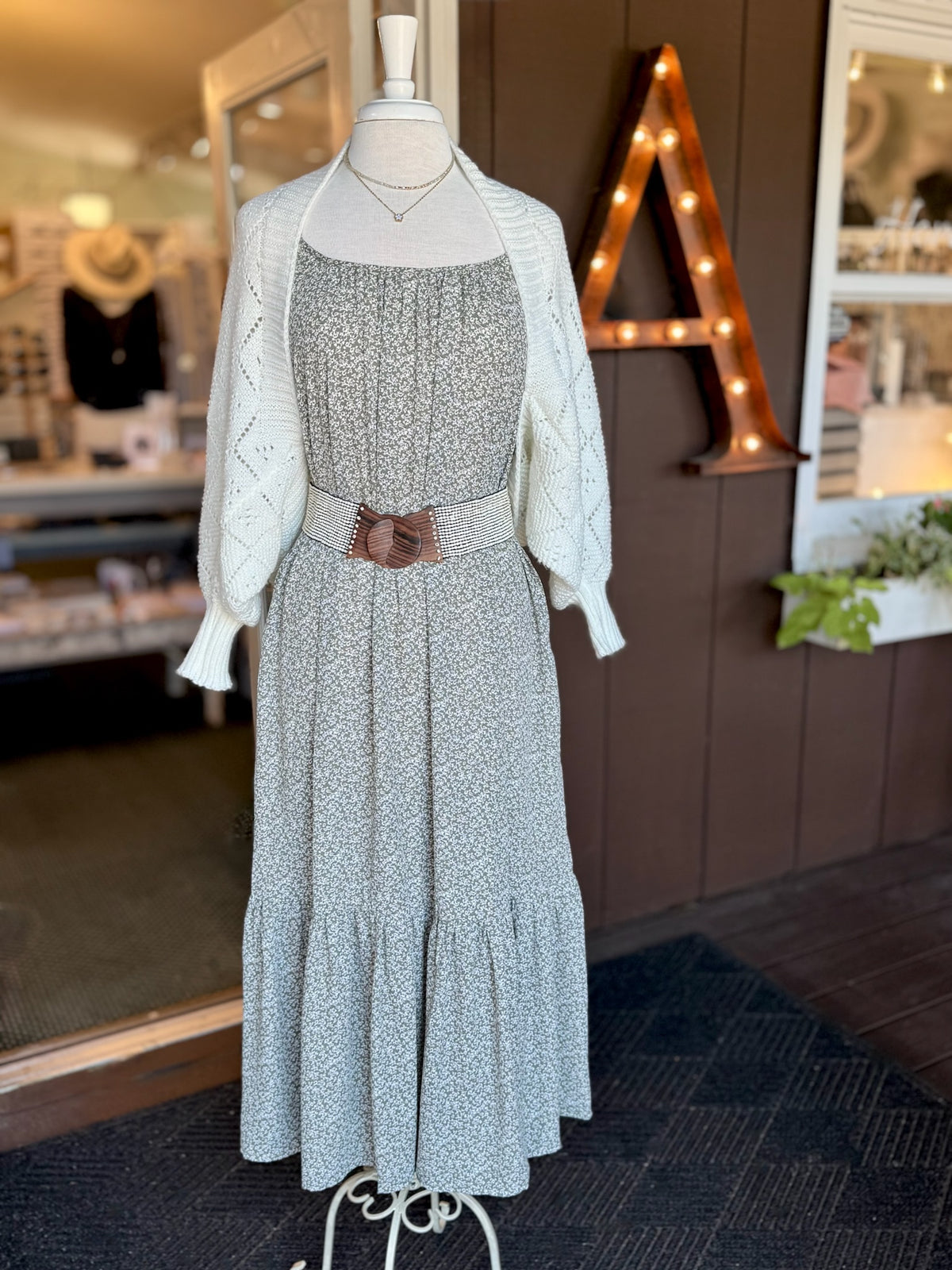 Olive green and white floral maxi dress styled with a cream open-knit cardigan and cream and brown waist belt for a layered transitional look at Ardor Boutique.