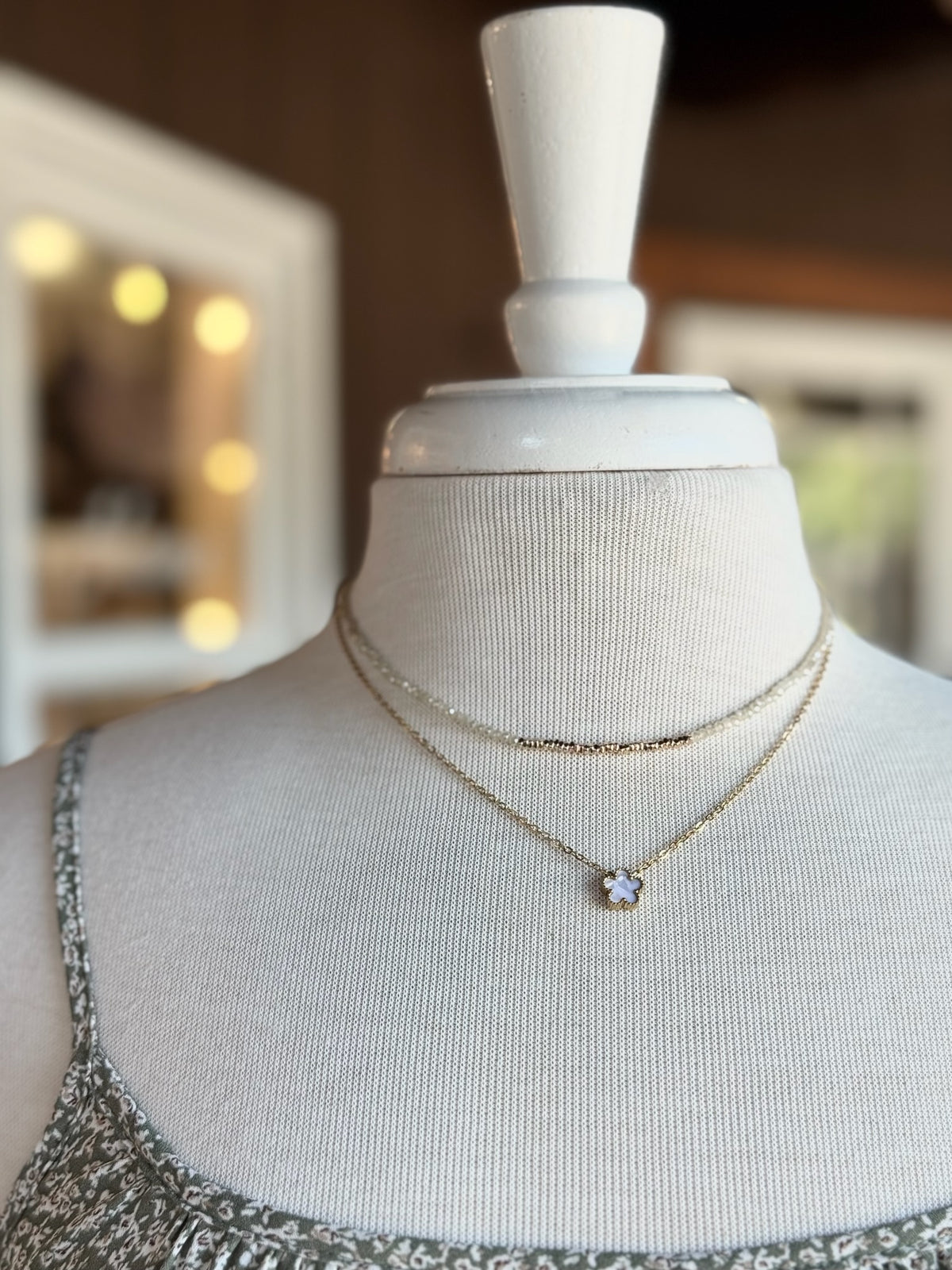 Neutral and gold beaded necklace layered with a delicate gold clover pendant necklace on a mannequin at Ardor Boutique.