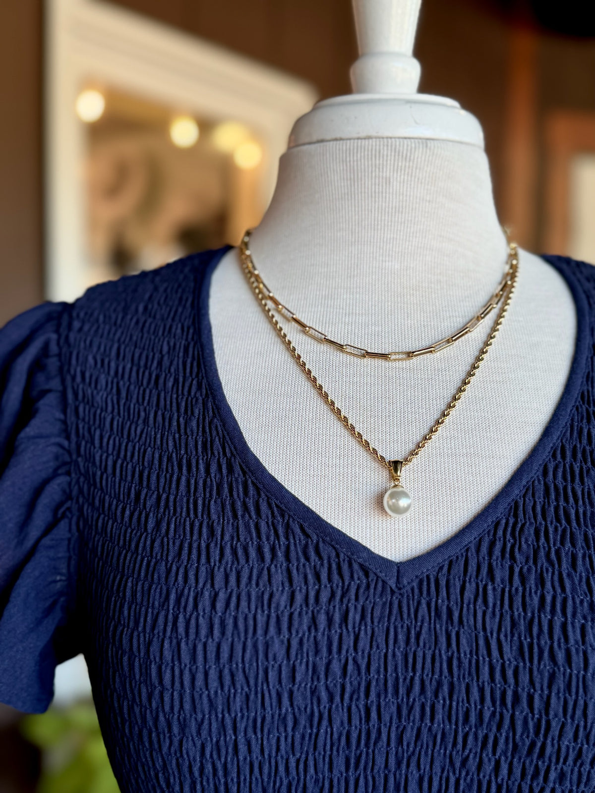 Gold rectangular link chain necklace layered with a gold pearl pendant necklace on a navy V-neck top at Ardor Boutique.