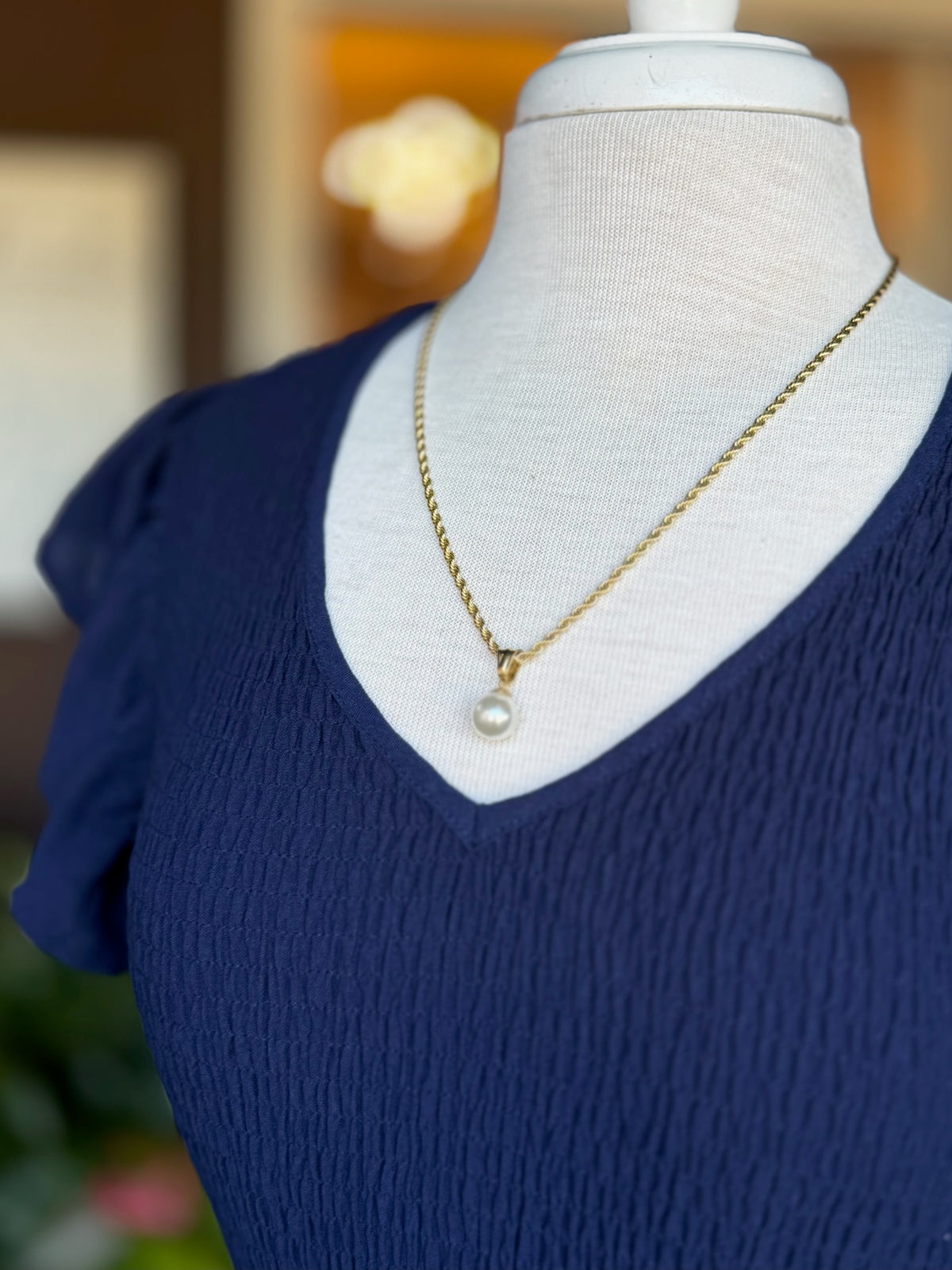Gold pearl pendant necklace chain on a navy V-neck top at Ardor Boutique.