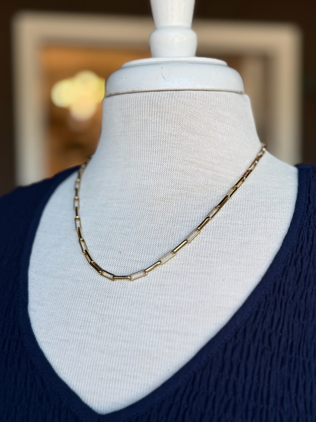 Gold rectangular link chain necklace styled alone on a navy V-neck top at Ardor Boutique.