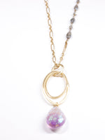 Close-up of gold and labradorite chain necklace with hammered oval rings and faceted amethyst teardrop pendant on white background.