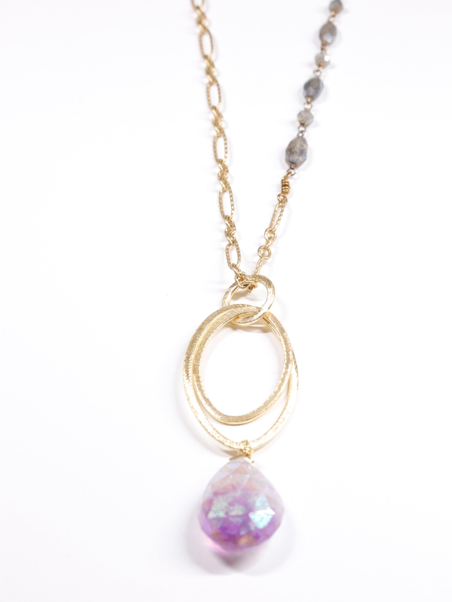 Close-up of gold and labradorite chain necklace with hammered oval rings and faceted amethyst teardrop pendant on white background.