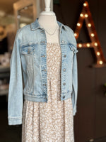 Light wash denim jacket layered over a beige and white floral dress with a delicate gold and pearl necklace, styled on a mannequin at Ardor Boutique.