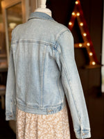 Back of the Light wash denim jacket layered over a beige and white floral dress styled on a mannequin at Ardor Boutique.