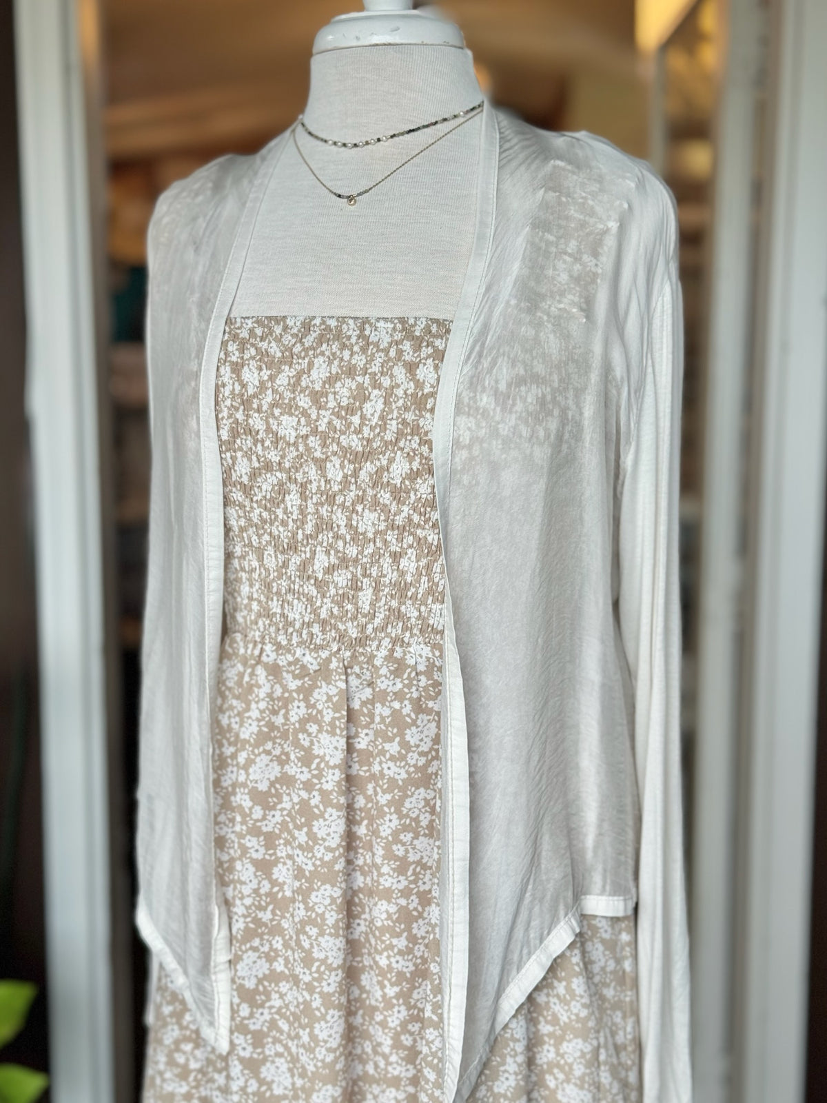 Ivory silk cardigan layered over a beige and white floral dress with delicate layered necklaces, styled on a mannequin at Ardor Boutique.
