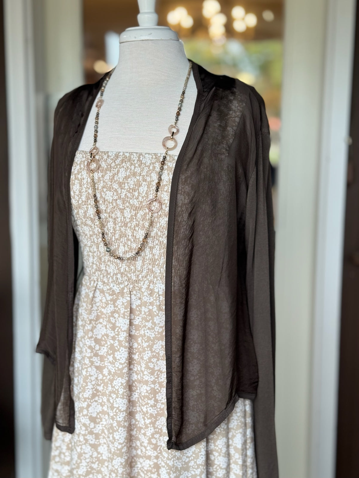 Brown lightweight semi-sheer open-front cardigan with long sleeves and a draped silhouette styled on a mannequin at Ardor Boutique.