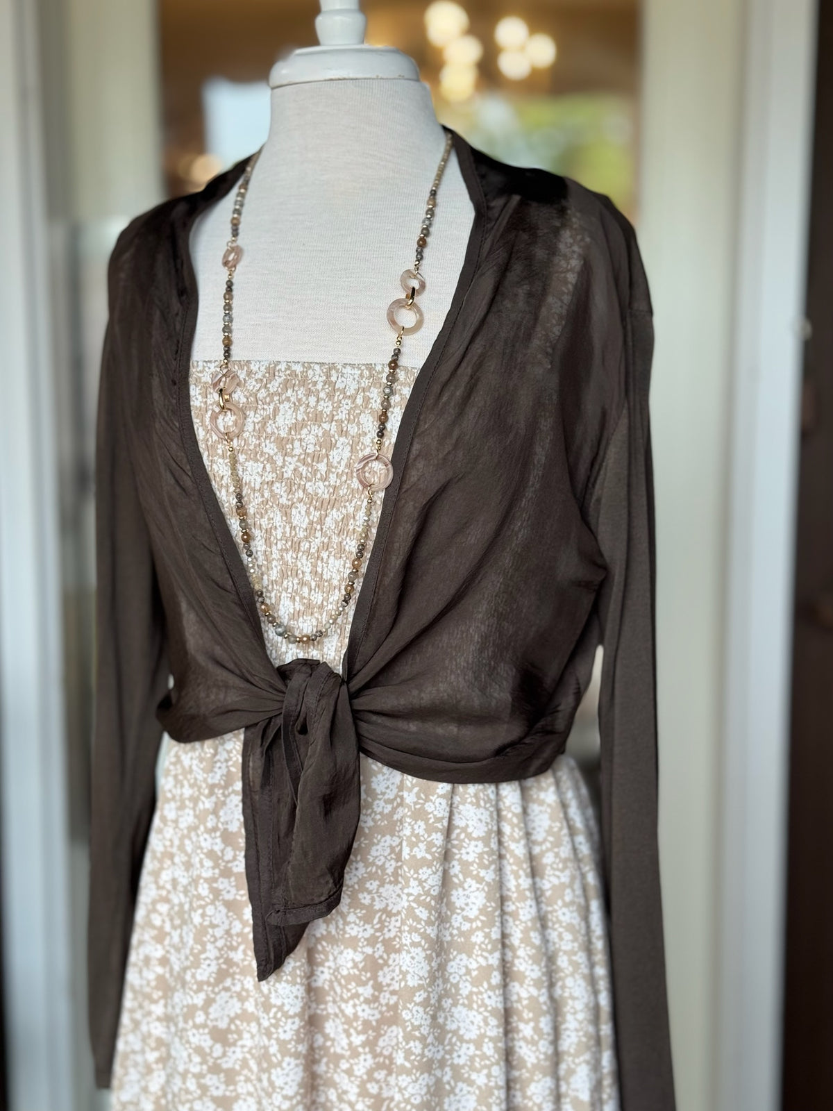 Brown lightweight cardigan styled tied at the waist over a neutral floral dress at Ardor Boutique.