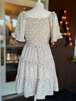 Back view of beige and white floral dress showing the smocked bodice, short flutter sleeves and tiered skirt at Ardor Boutique.